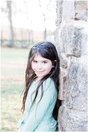 Young person in mint sweater leaning against stone wall outdoors.