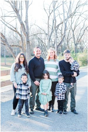Family group portrait outdoors with bare trees in background during winter.