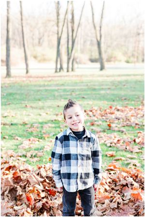 Child in plaid shirt standing among fallen autumn leaves in park setting.