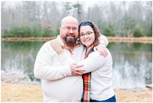 Couple in cozy sweaters posing together by a lake in autumn.