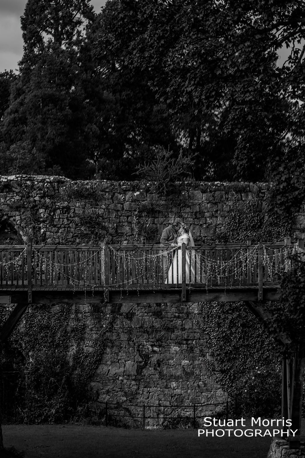 bride and groom kiss on the rustic wooden bridge in the grounds at Ruthin castle Stuart Morris Photography
