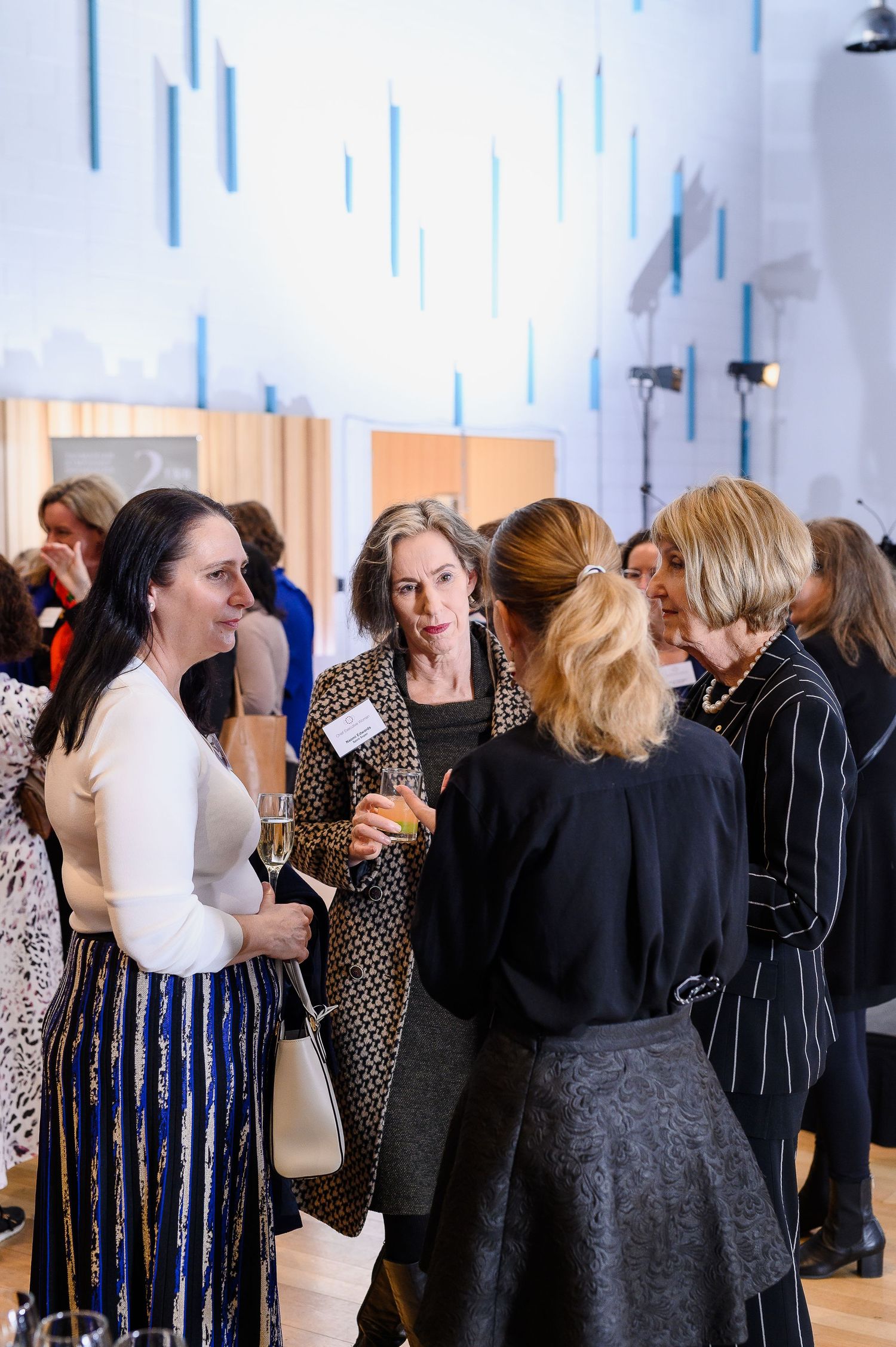 Elegant networking event with attendees gathered in conversation near blue wall accents.