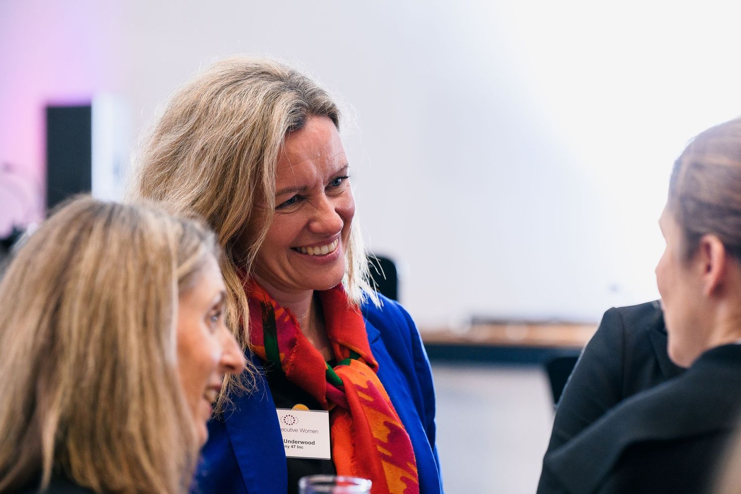 Professional networking event shows attendees engaged in animated conversation wearing business attire.