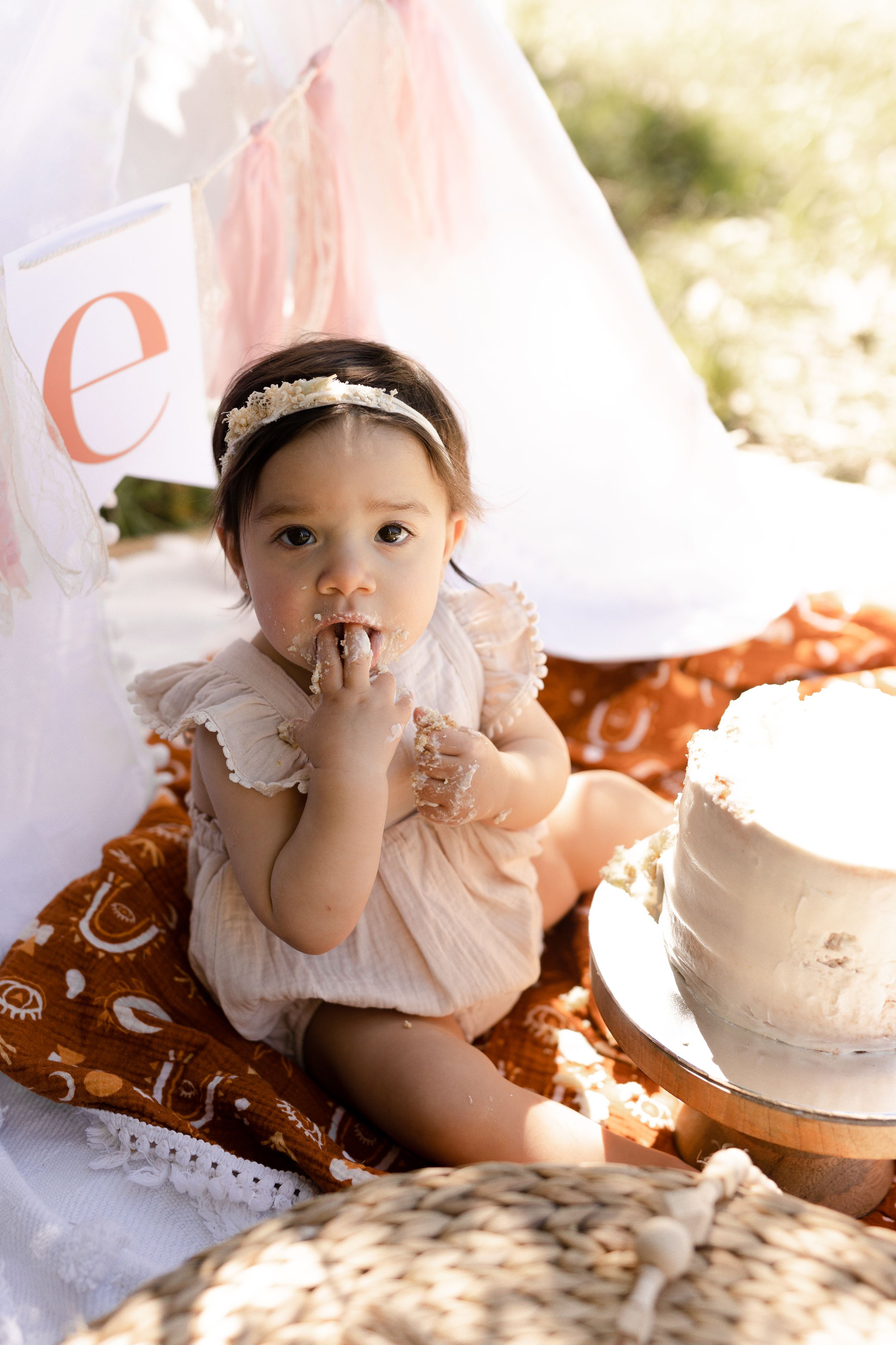 Baby in white ruffled dress lying on blanket during outdoor photoshoot.
