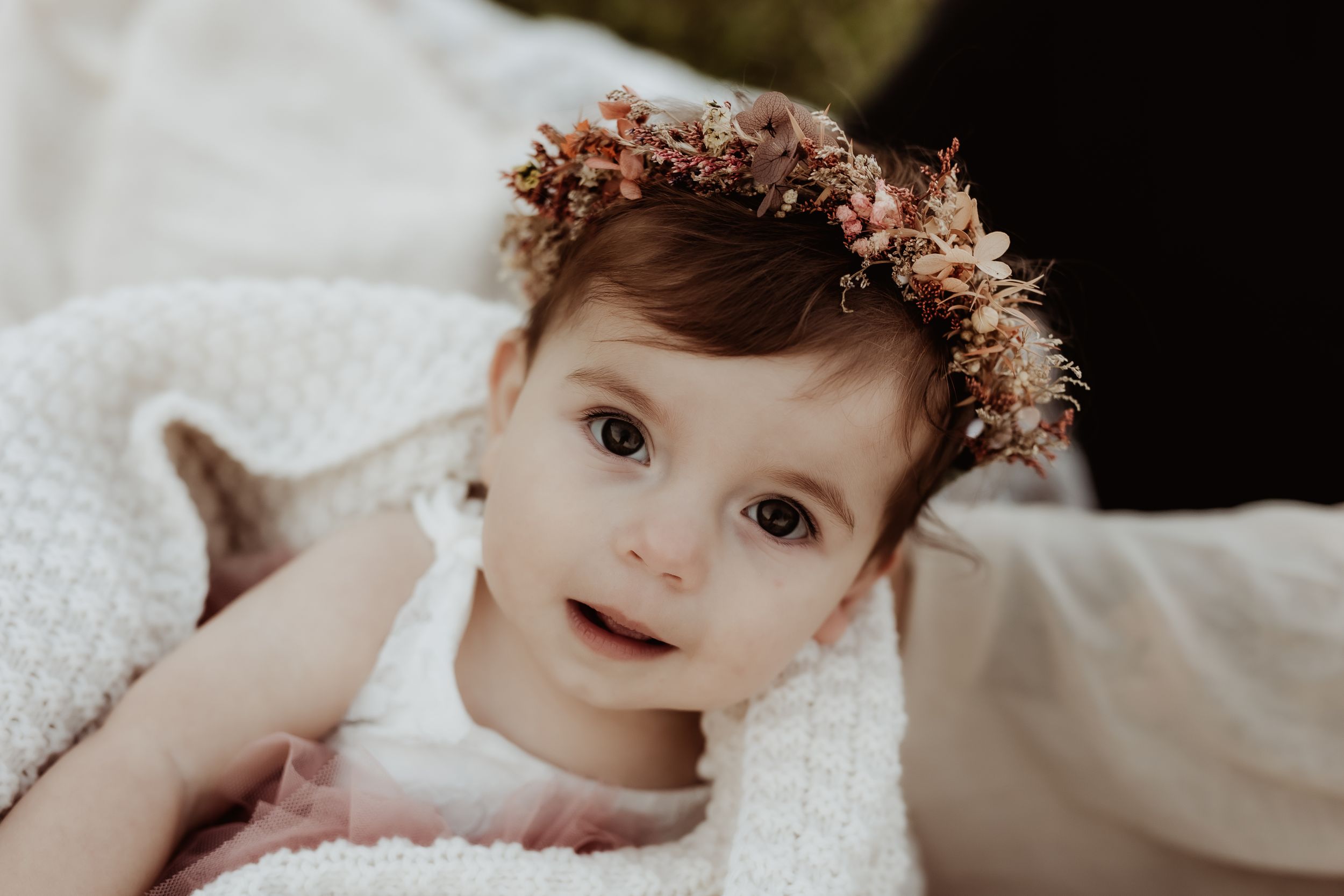 Sweet portrait of baby wearing floral crown against light background.