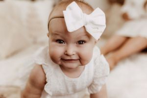 Sweet baby portrait with white bow headband in soft sepia tones.