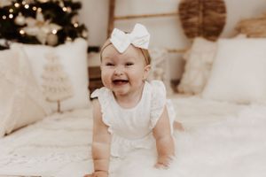 Baby in white ruffled outfit smiling during holiday photoshoot.