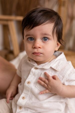 Baby in white button-up shirt sitting with large expressive eyes.