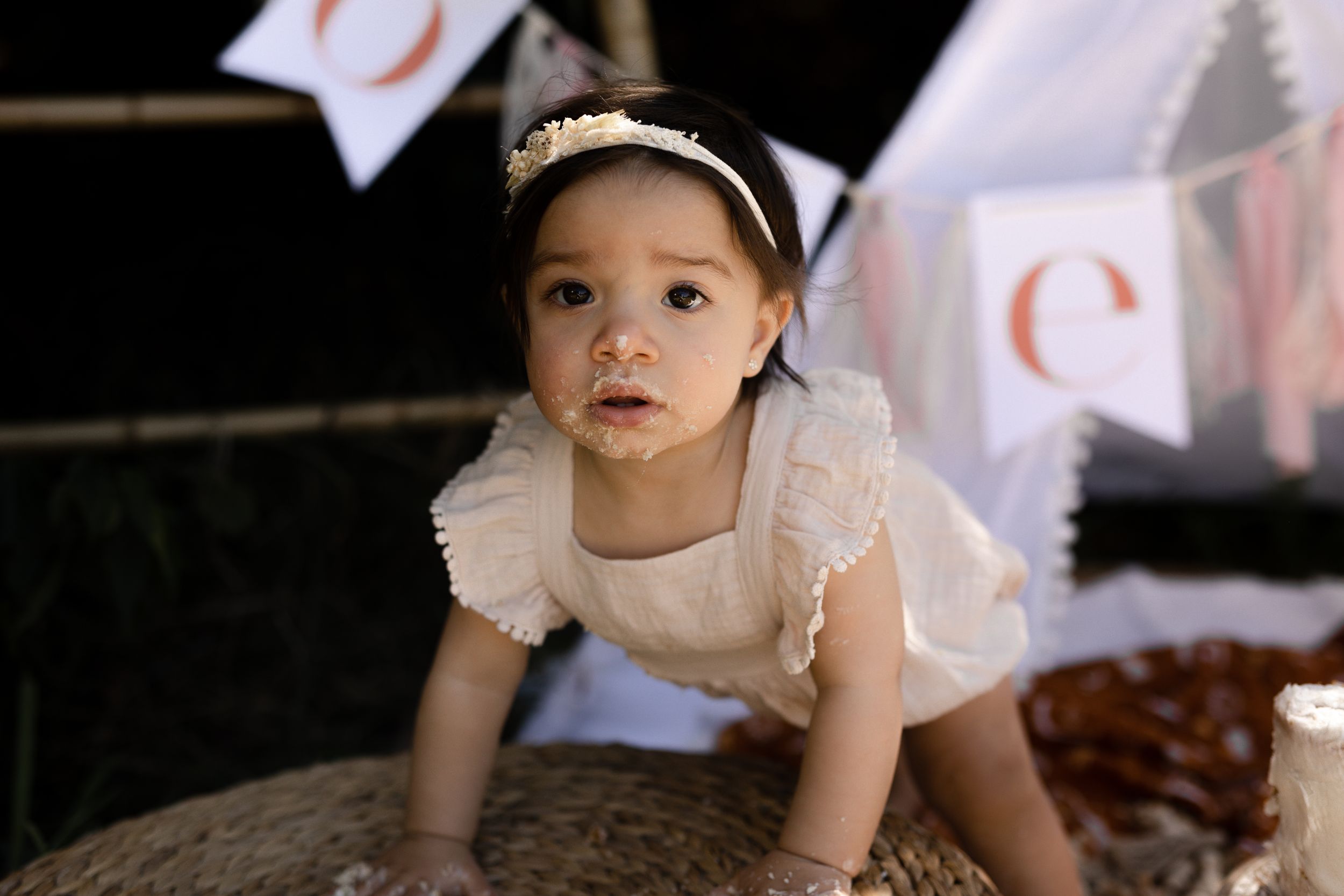 Baby in delicate white dress exploring during an outdoor portrait session.