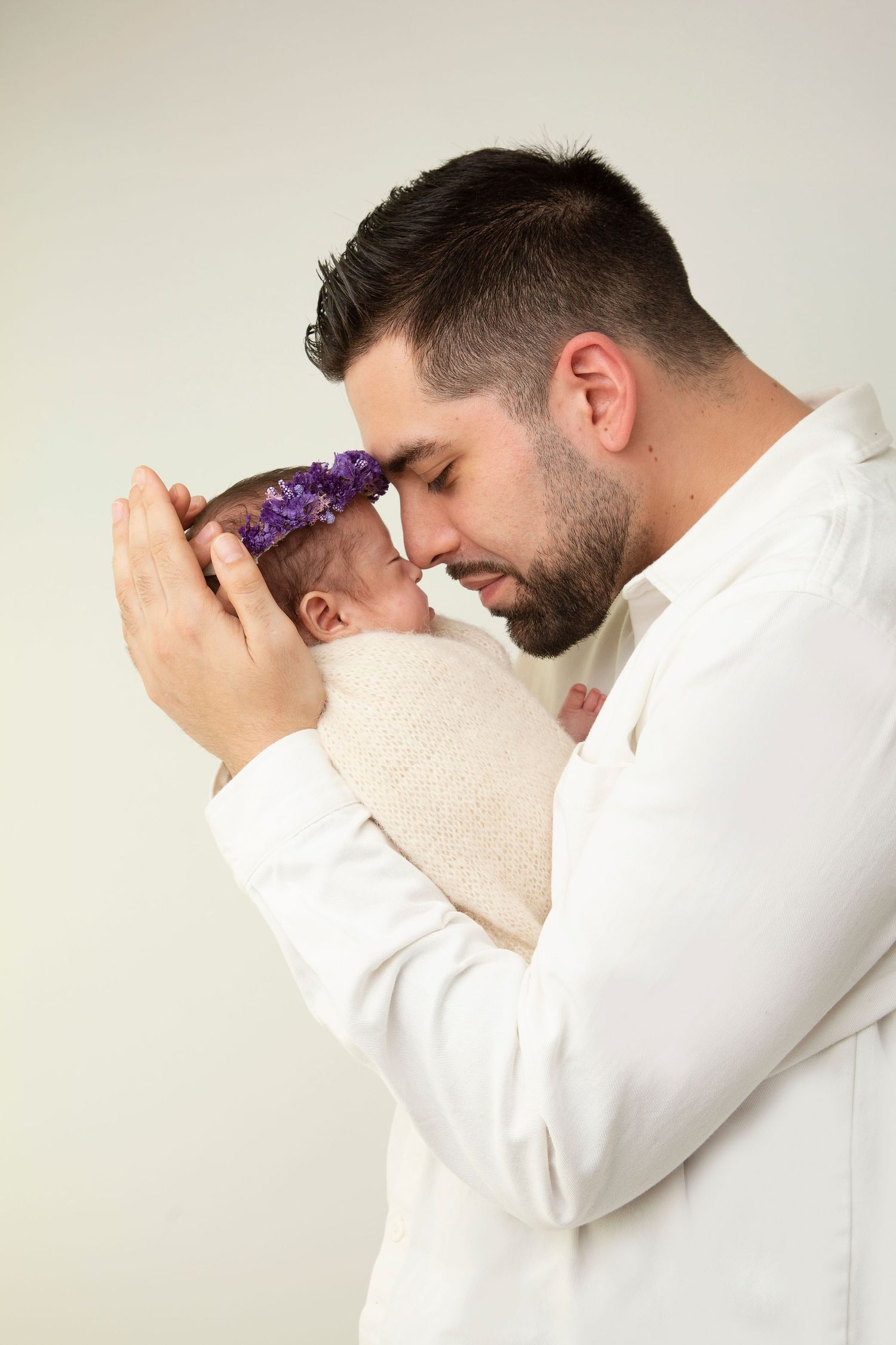 A tender moment between parent and baby wearing a purple headband in white studio setting.