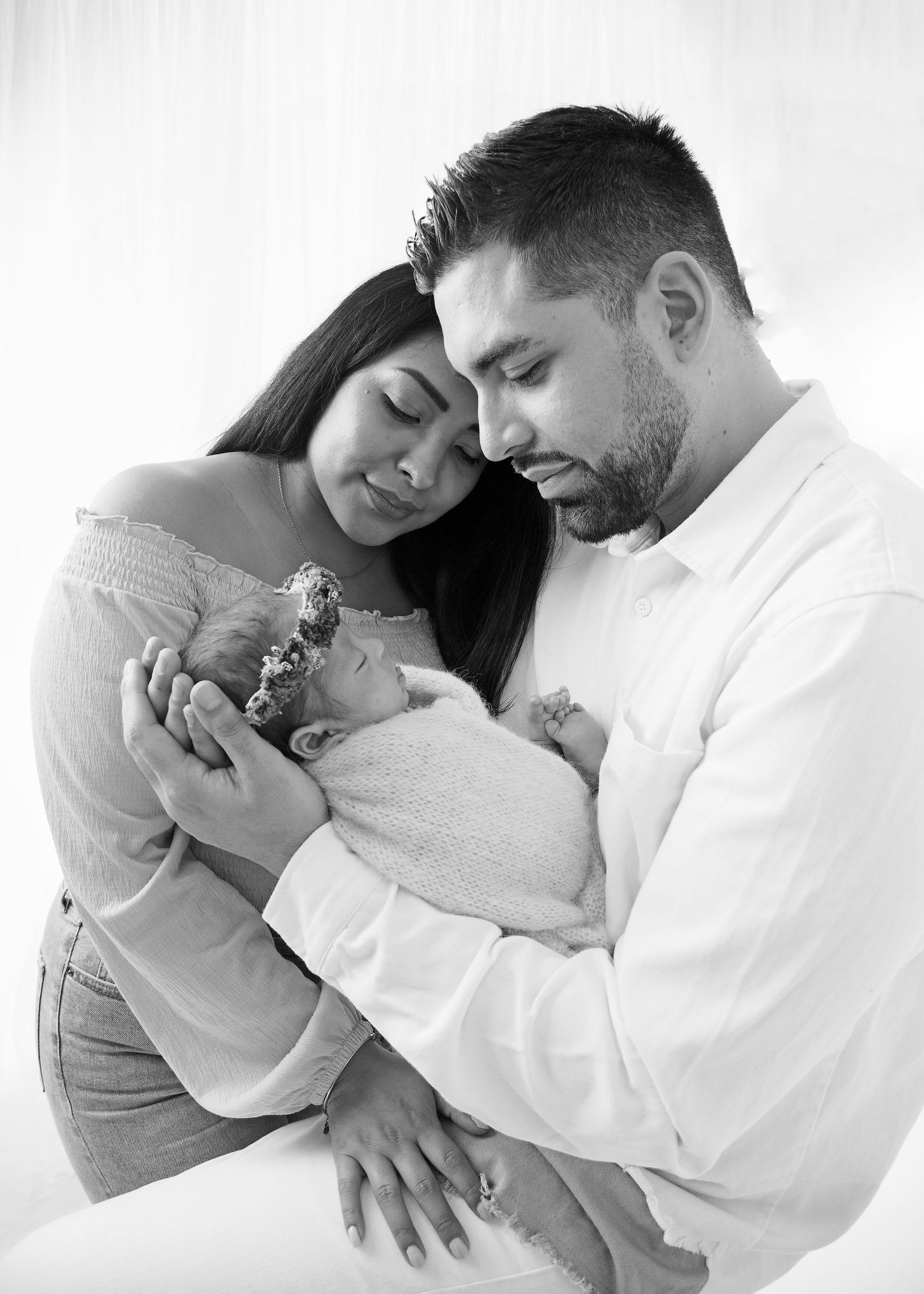 A couple tenderly embraces their newborn baby in a sweet black and white portrait.