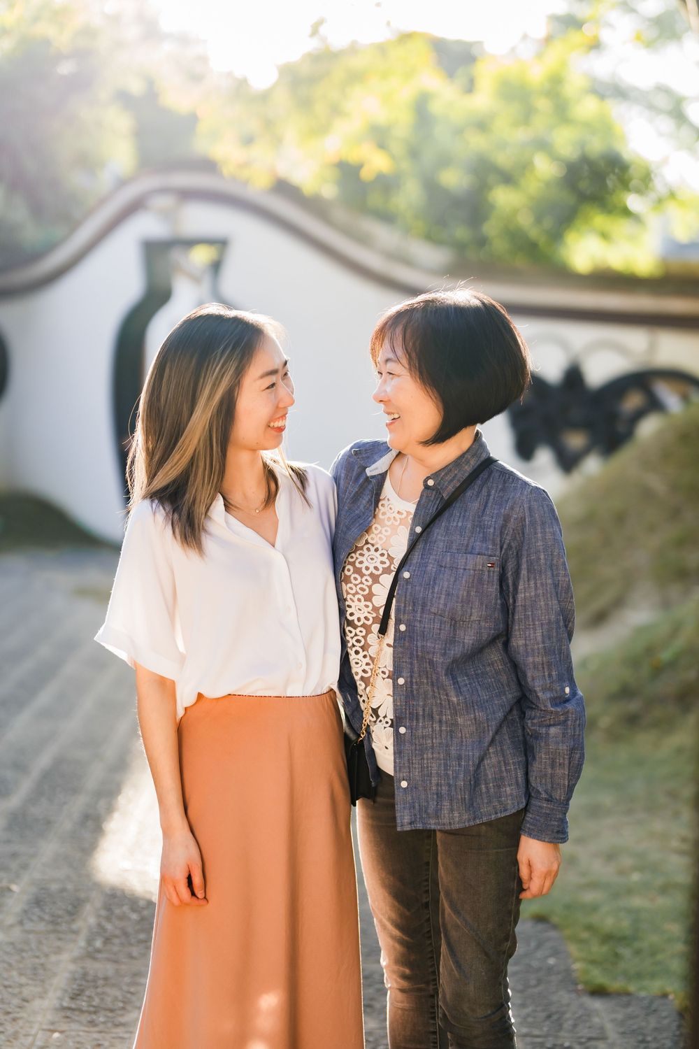 Two women in casual attire sharing a warm moment along a traditional Chinese garden wall.
