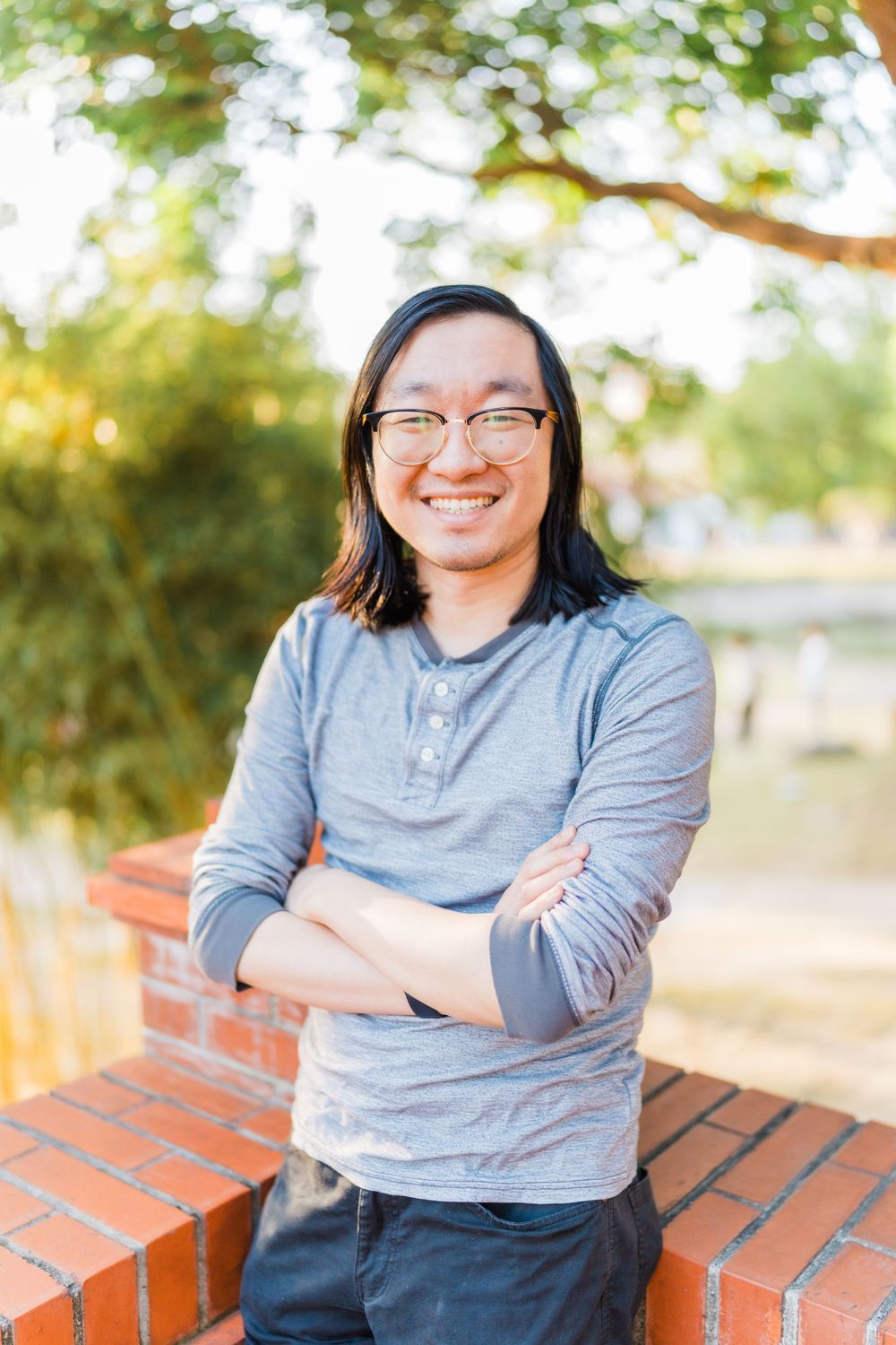 Portrait of a person in casual attire smiling warmly against a sunlit outdoor background.