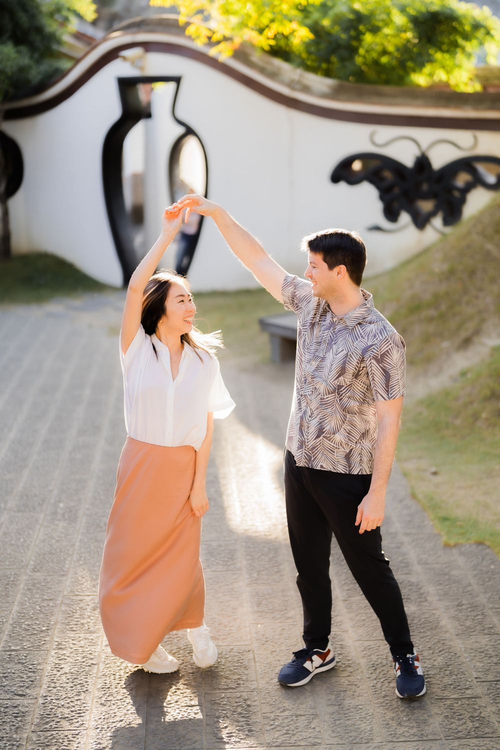 A couple dancing and twirling together on a path with decorative walls in the background.