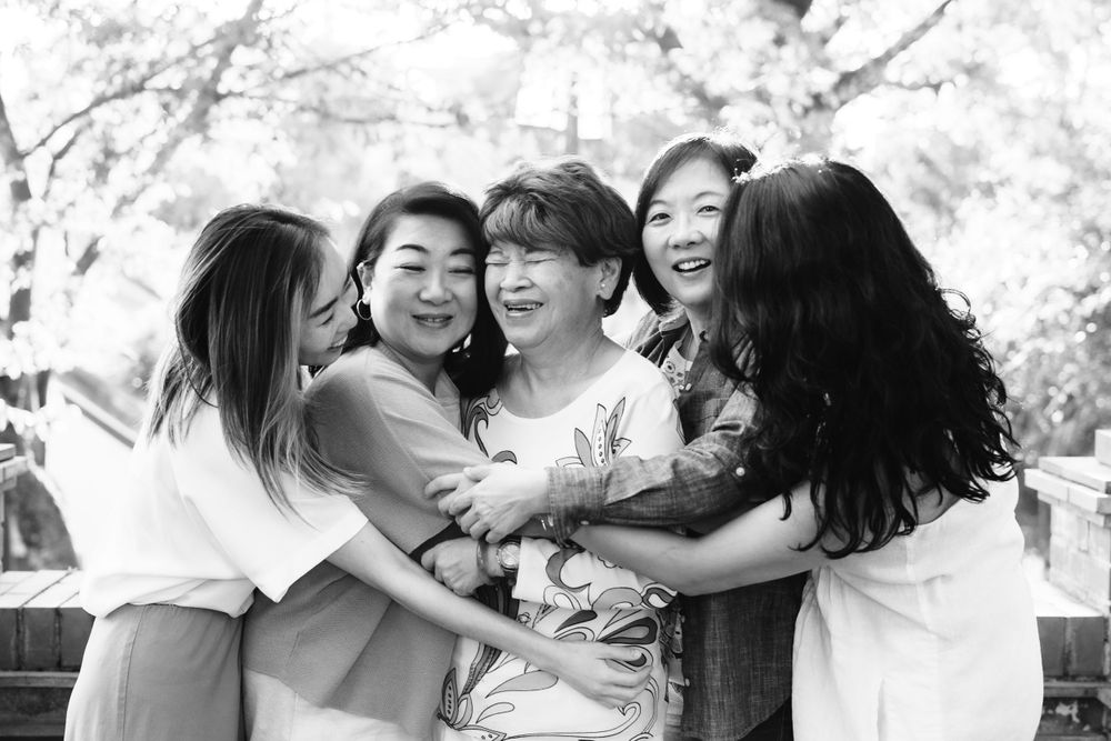Black and white photo of a family sharing an affectionate group hug in a park setting.