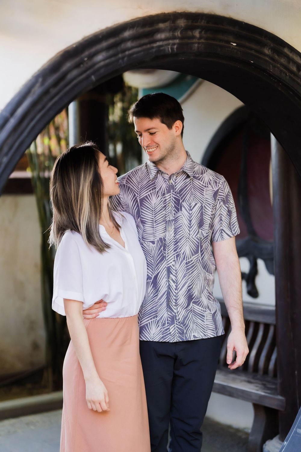 A couple sharing a romantic moment under an arched doorway wearing complementary casual outfits.