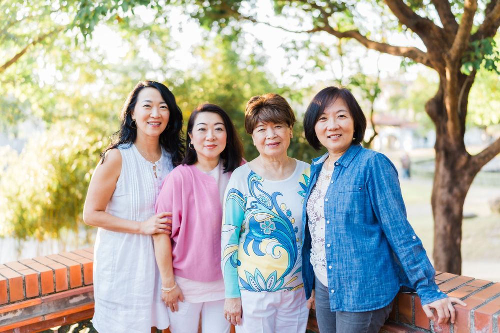 Four friends in casual attire pose together outdoors under green trees.