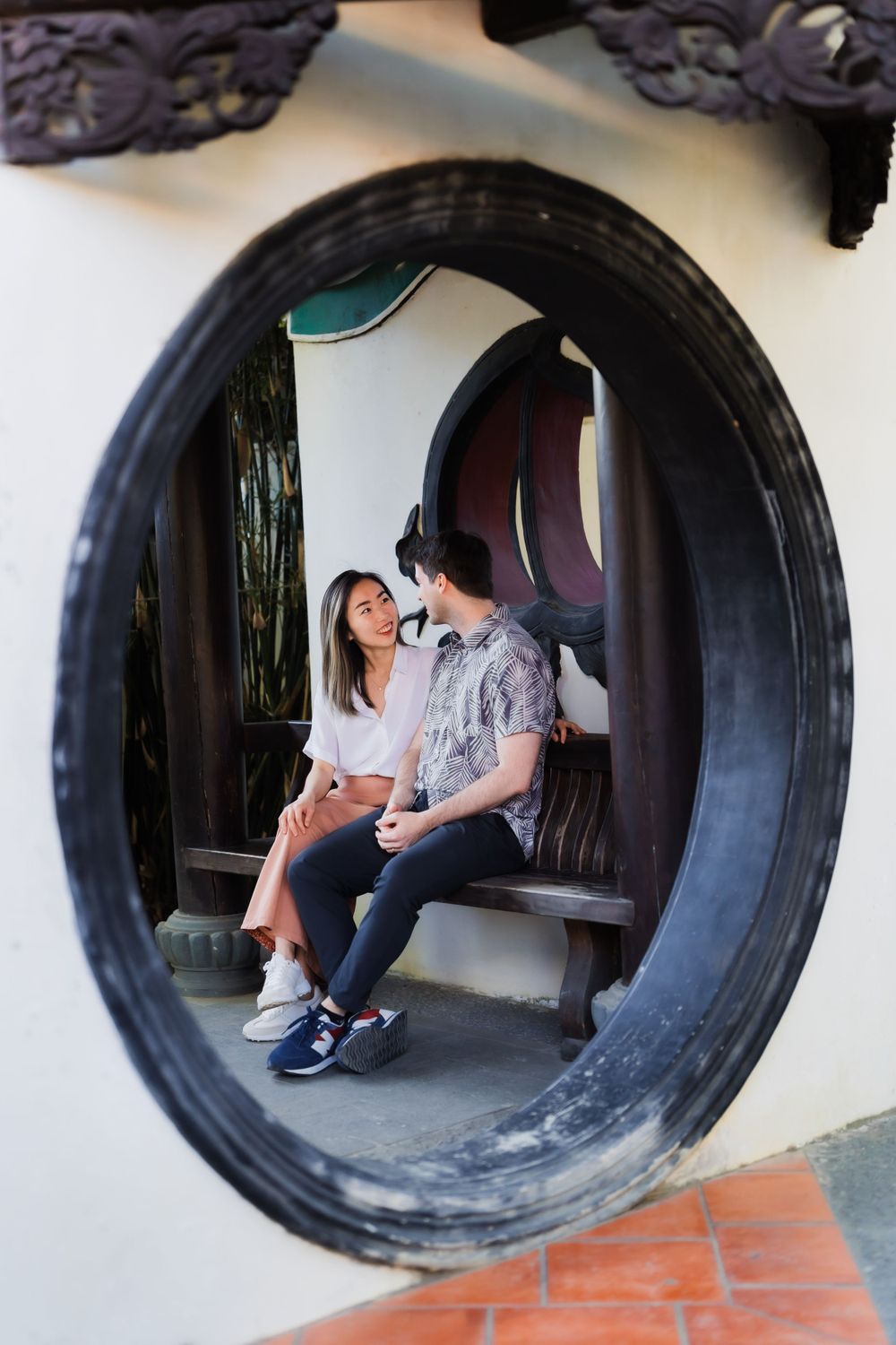 A framed view through a circular window of a couple sitting together on a bench.