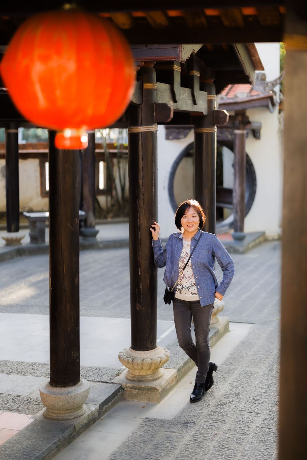 A casual portrait beneath a red Chinese lantern in a traditional courtyard setting.