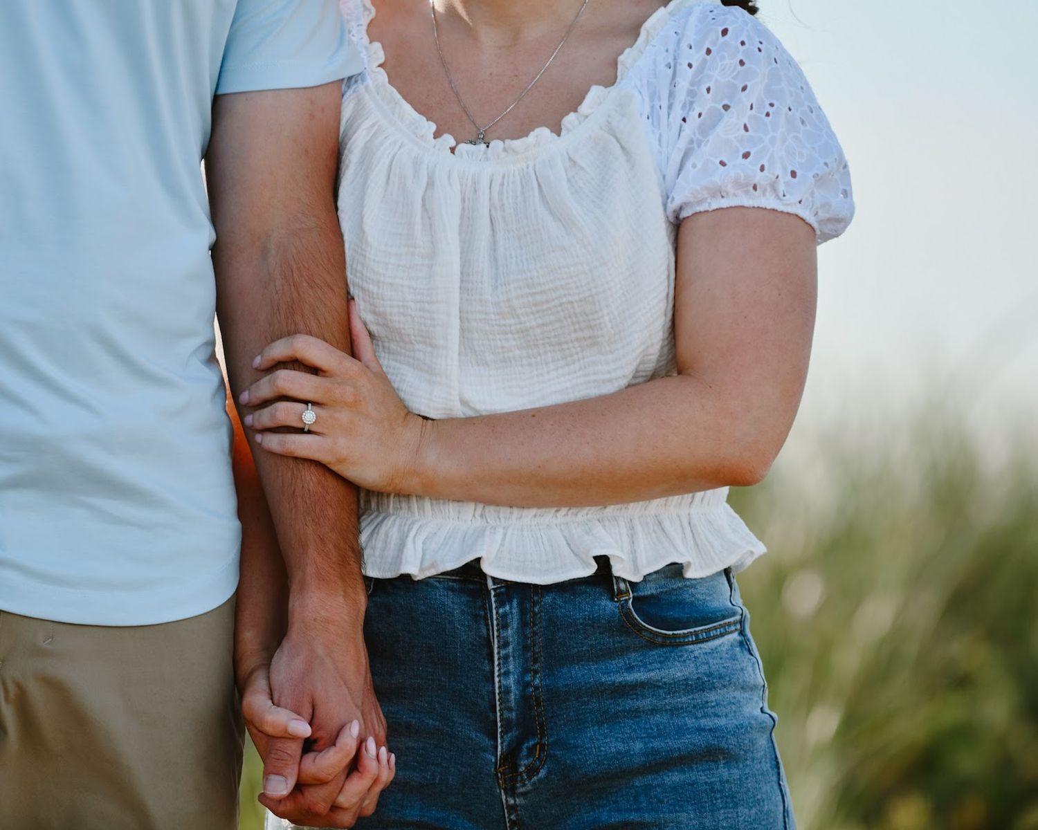 A romantic couple holds hands while wearing casual white tops and jeans in an outdoor setting.