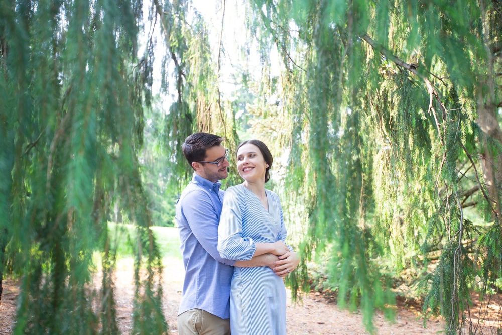 Happy couple embracing under weeping willow branches in a sunny green park setting.