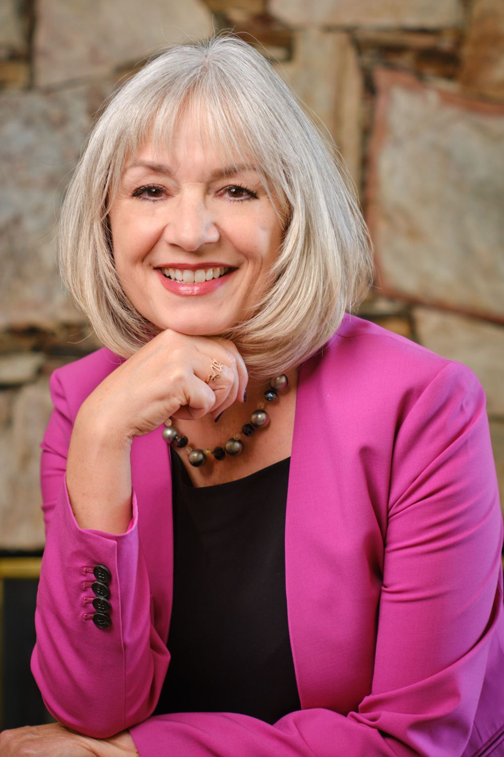 Professional headshot of a person wearing a vibrant pink blazer and statement necklace.