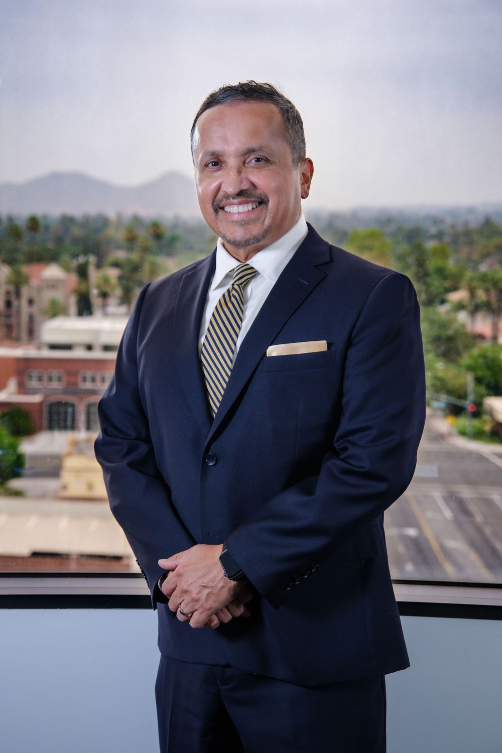 Professional business portrait of a person in navy suit and striped tie against city backdrop.