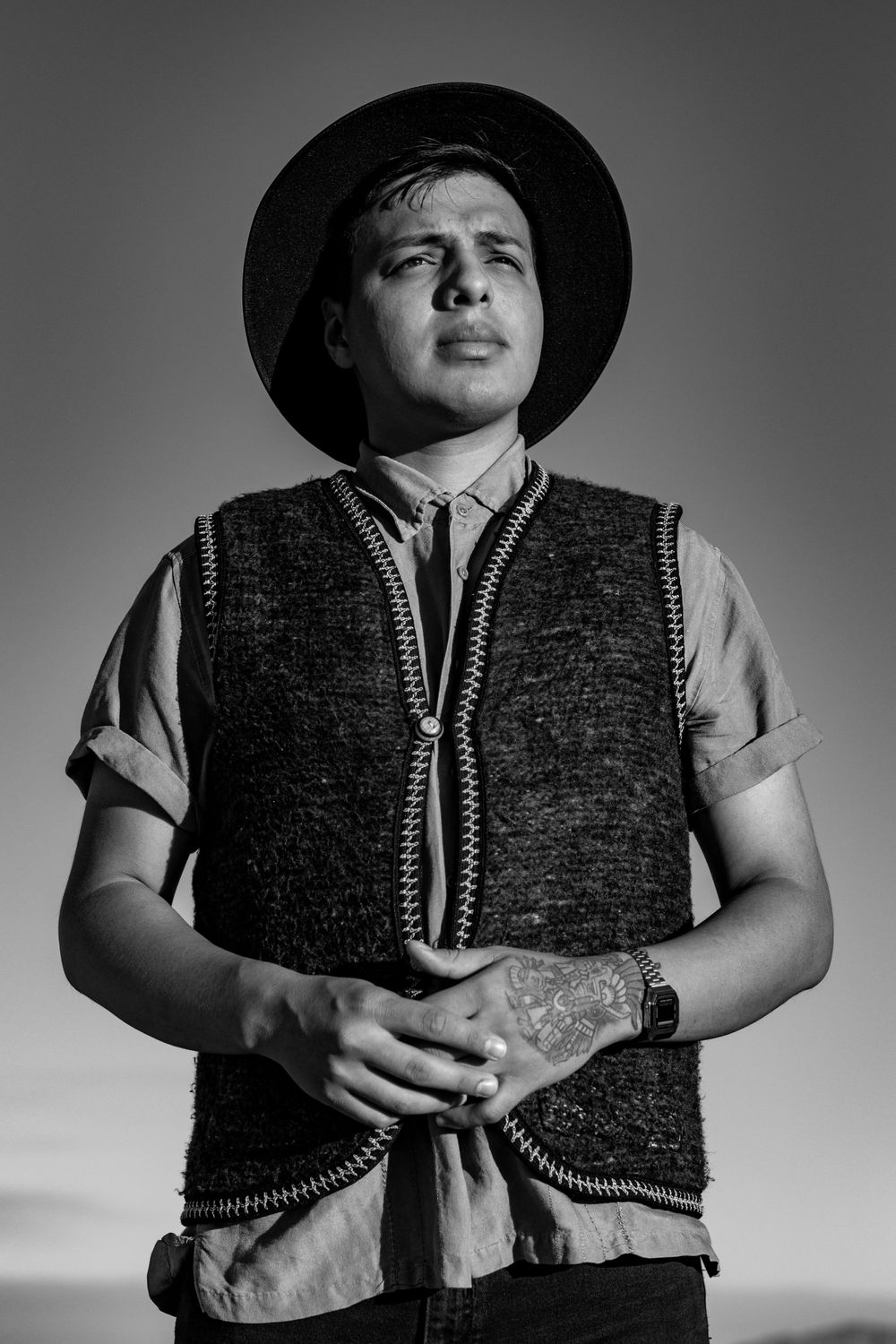 Artistic black and white portrait of person wearing vintage vest and hat against dramatic lighting.