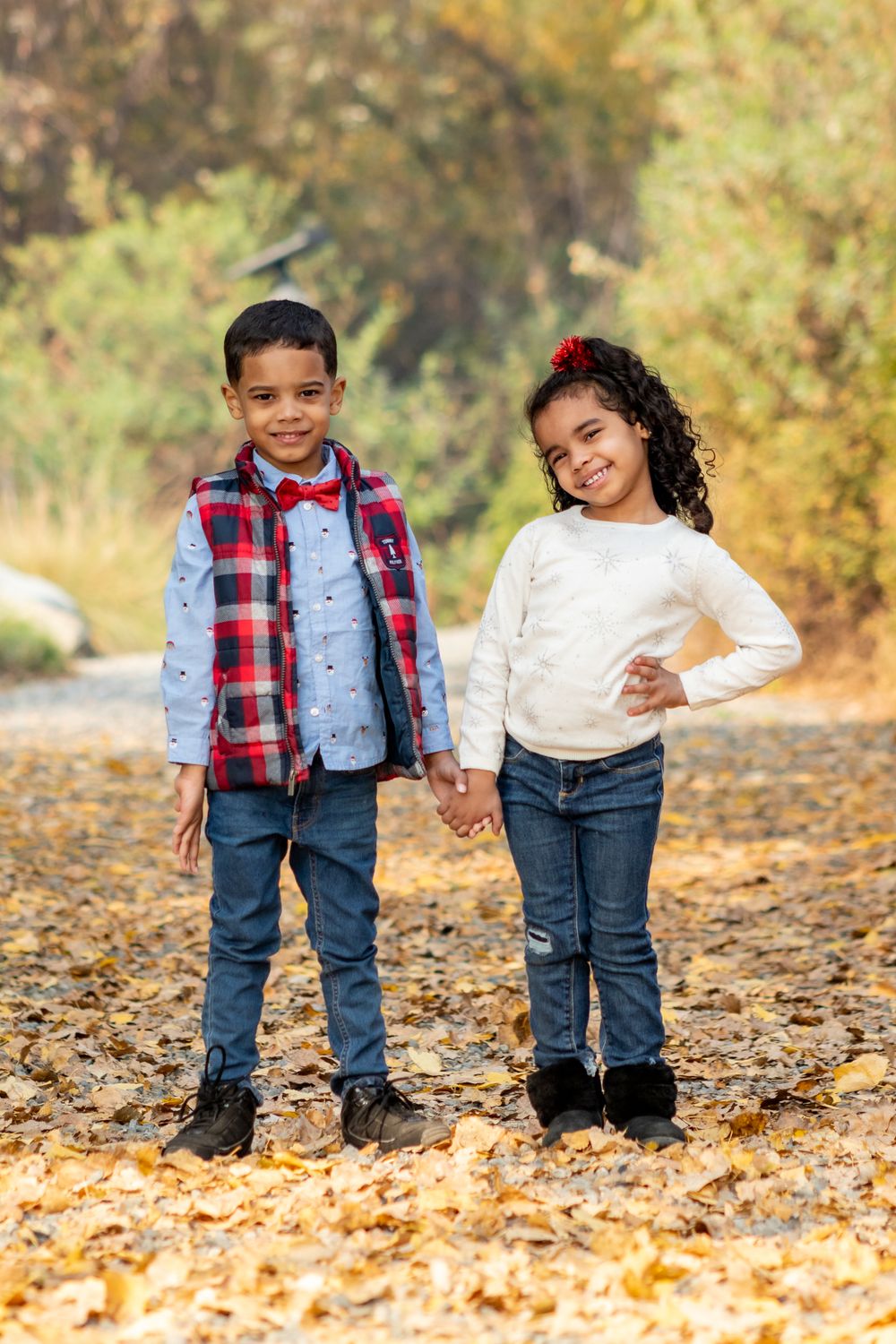 Two children posing together on autumn pathway covered in fallen leaves.
