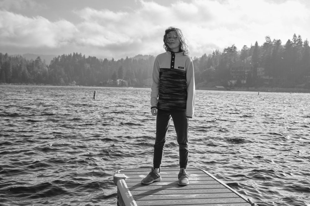 Person standing on a wooden dock overlooking a serene lake surrounded by forest.