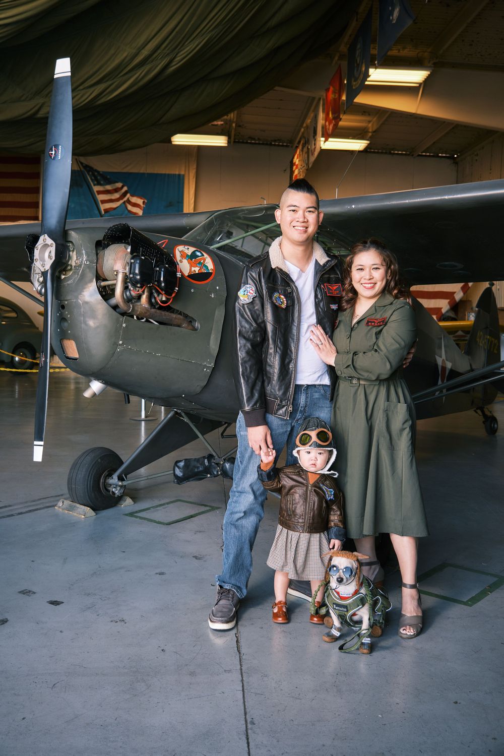 Family posing with their dog in front of a vintage aircraft in a hangar.
