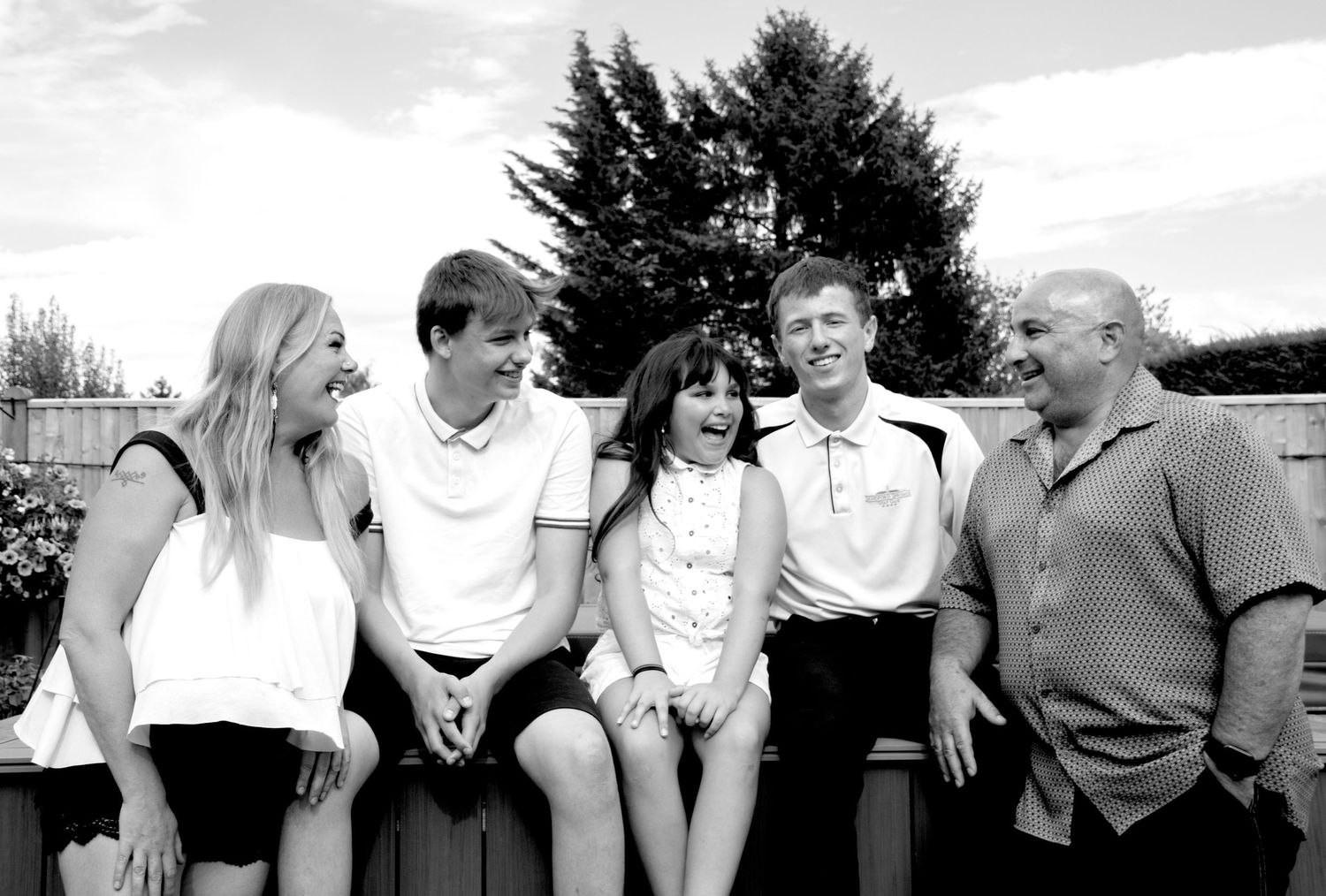 Happy family of five sitting together outdoors laughing in a candid black and white portrait.