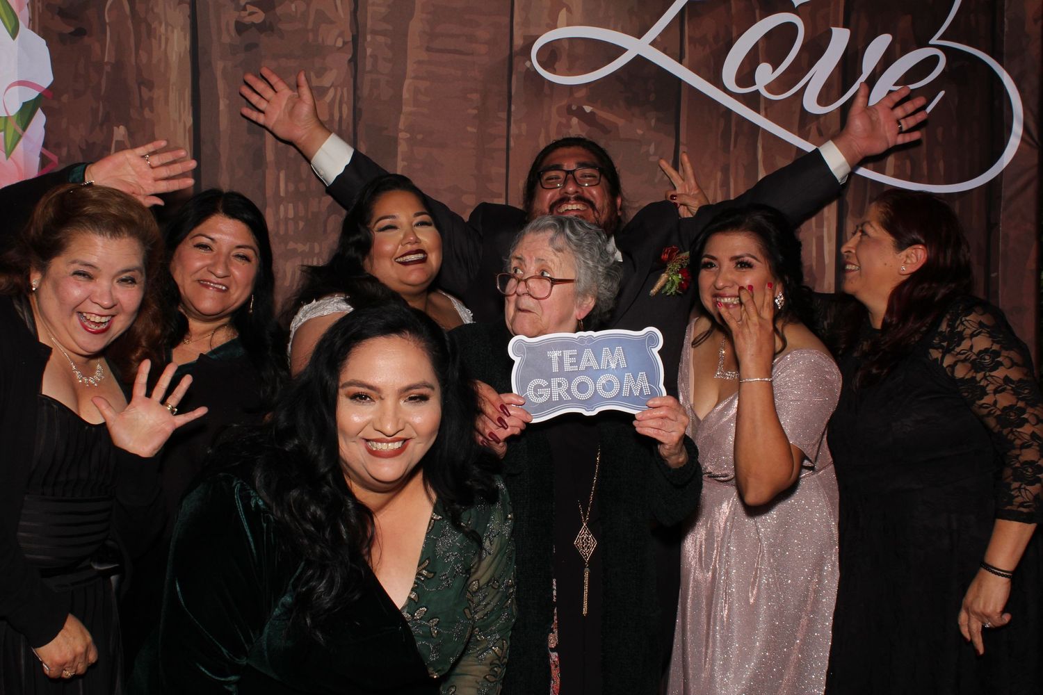 A group of friends pose together at a party with a 'Love' sign on the wall behind them.