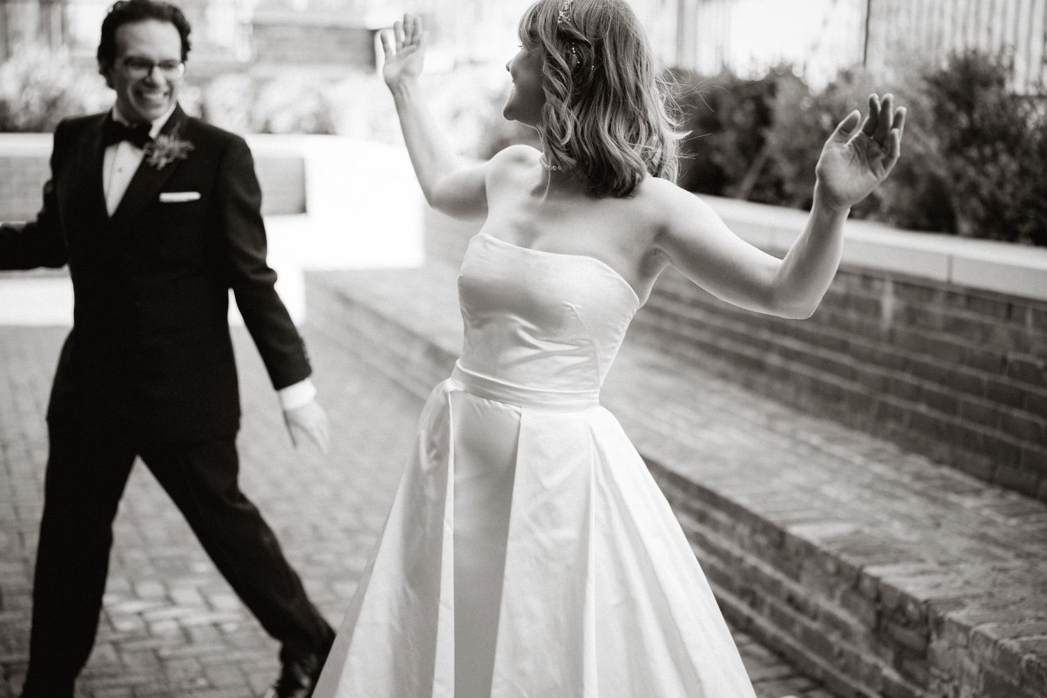 Black and white photo of a couple dancing playfully on outdoor stone steps.