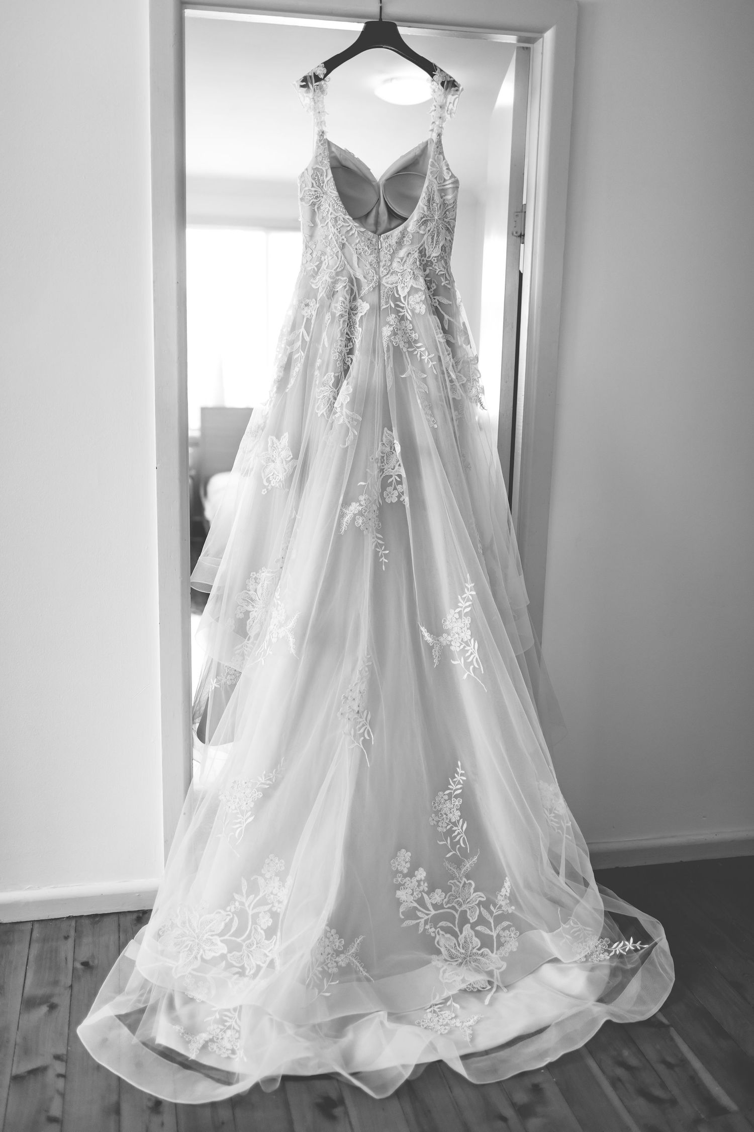 Elegant white lace wedding gown with floral details hanging on display.