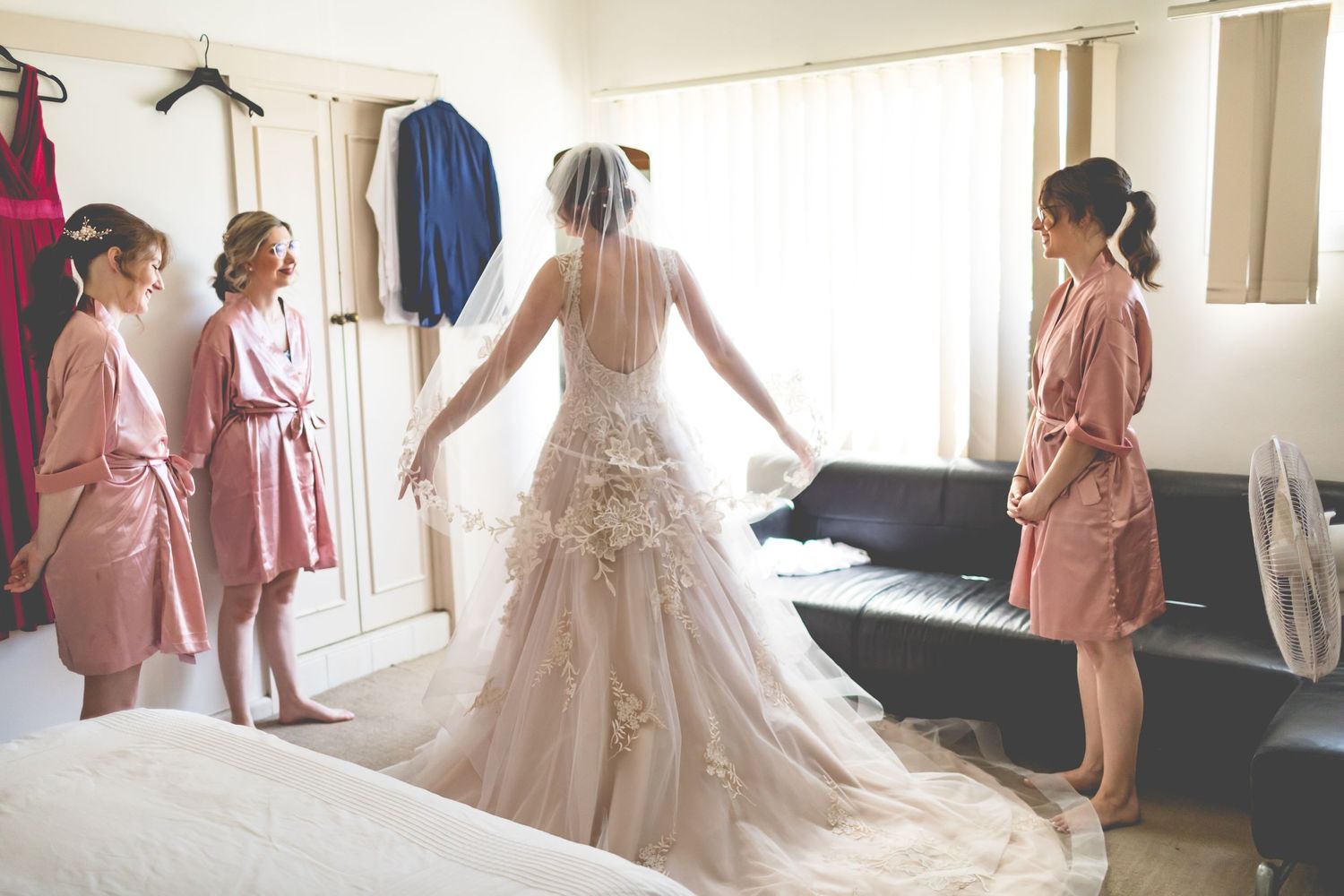 Wedding preparation scene with bride in flowing dress surrounded by attendants in robes.