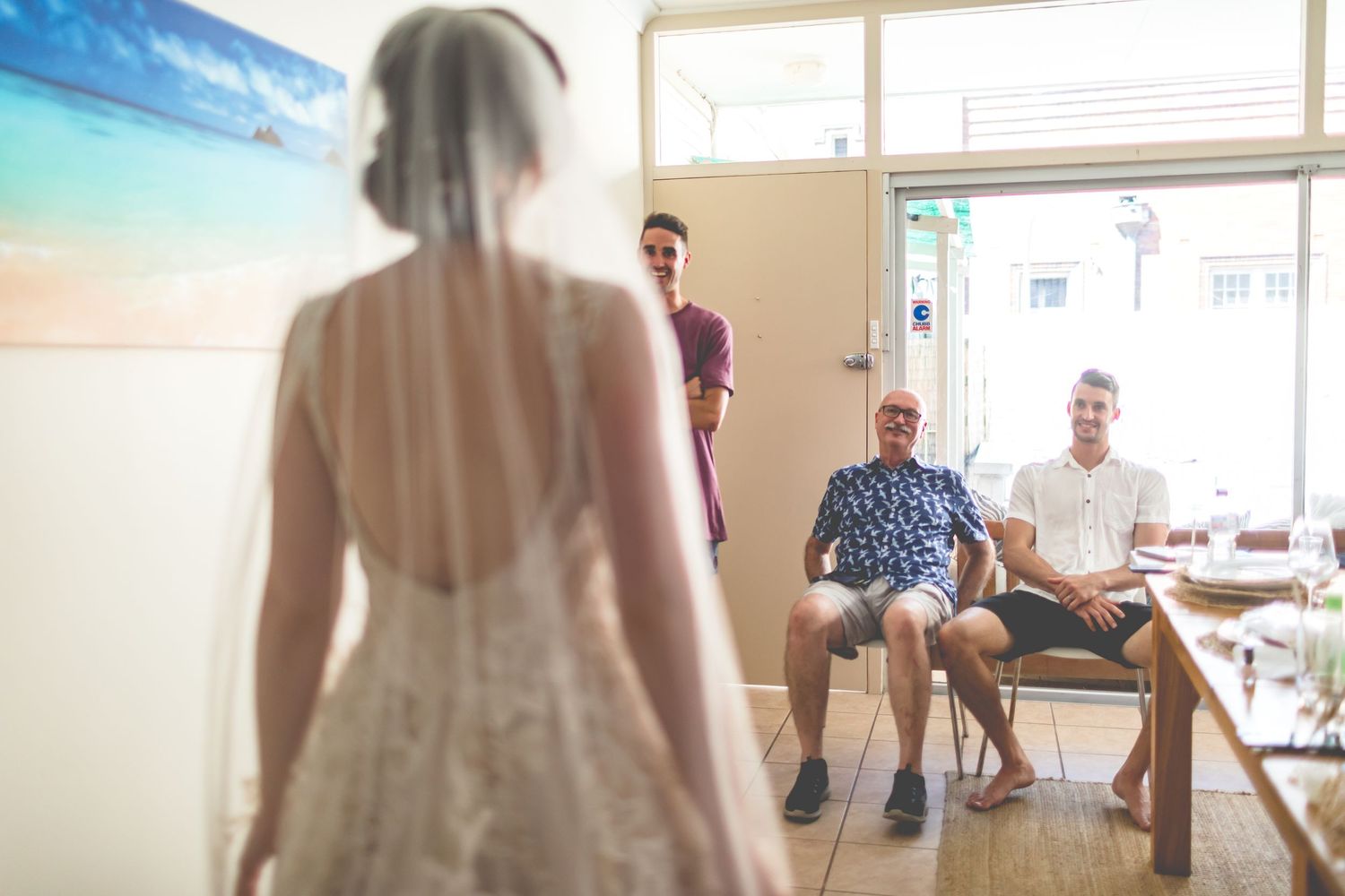 Bride in wedding dress showing off gown to seated guests in bright room.
