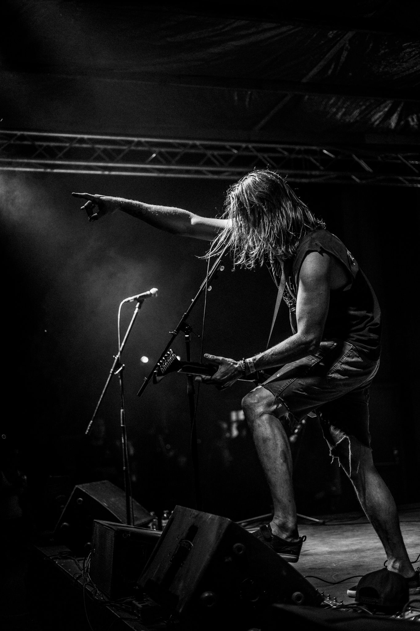 Silhouetted metal musician with long hair performs energetically on dark stage.