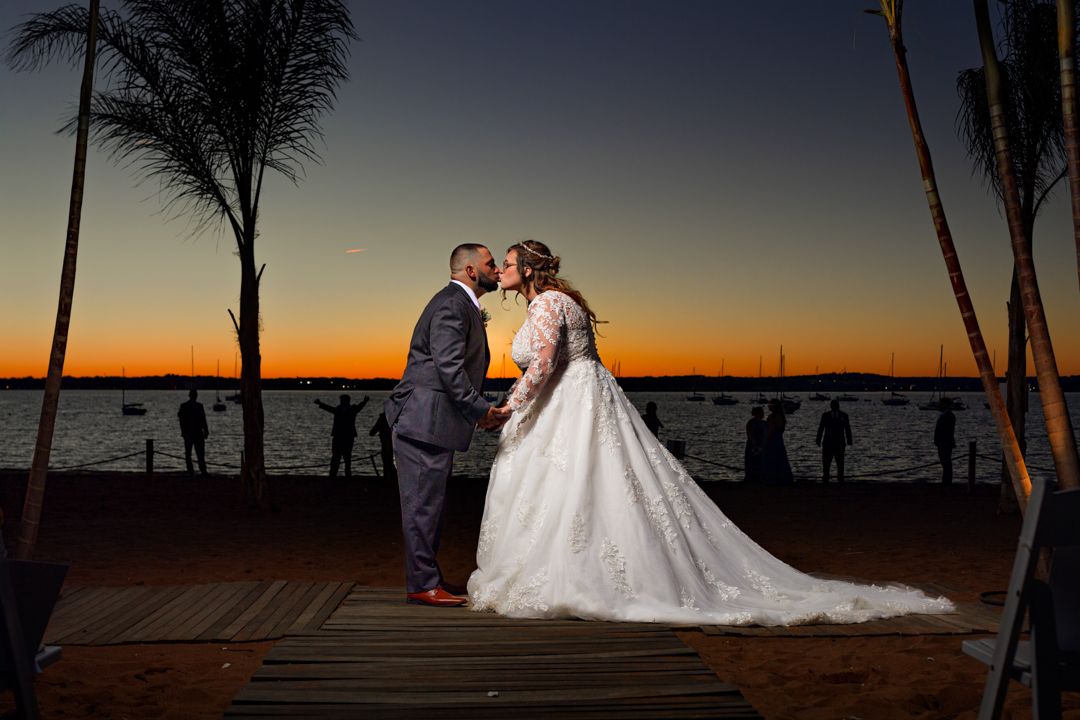 A romantic sunset wedding moment with palm trees silhouetted against an orange sky.