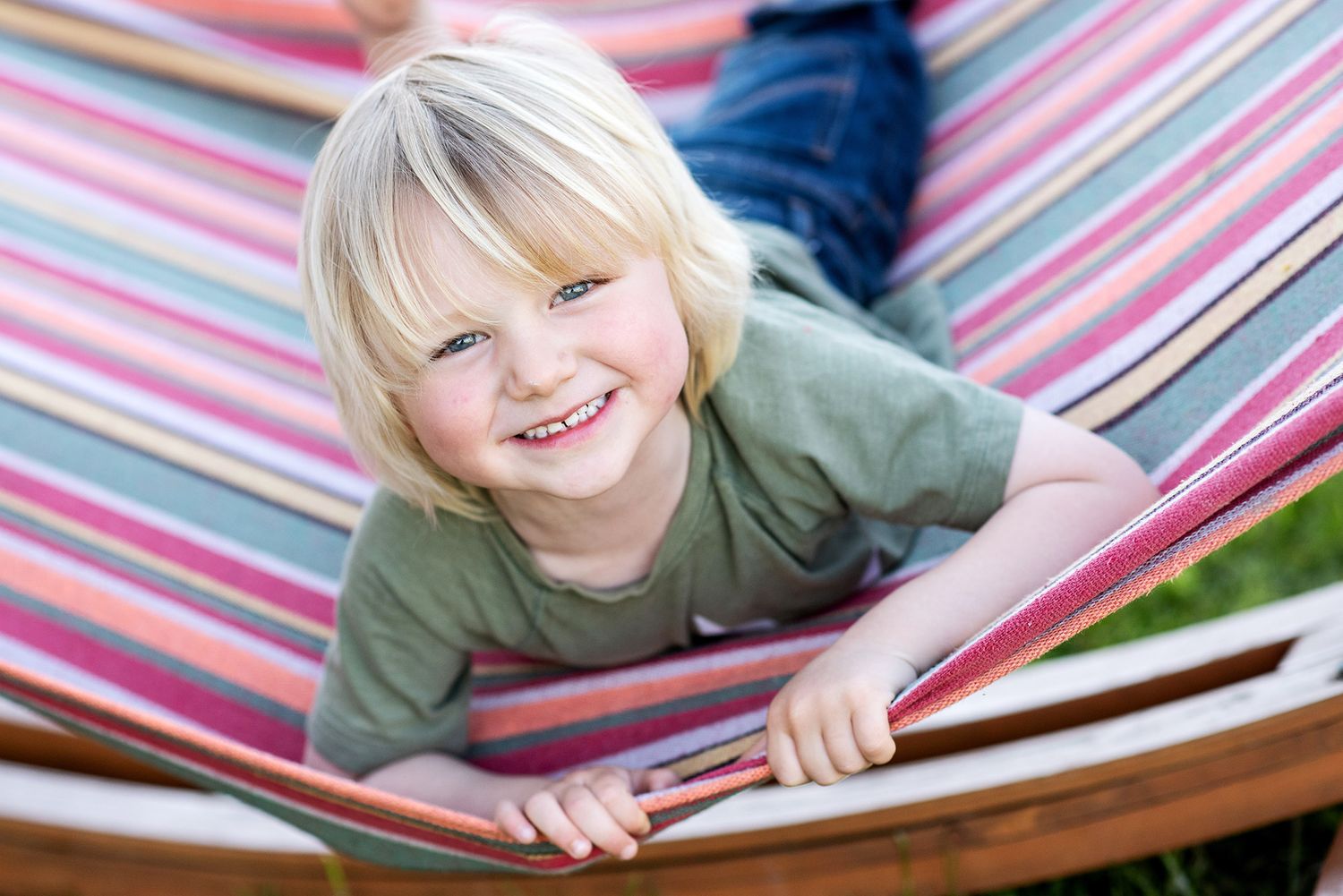 Child relaxing in a colorful striped hammock with a bright smile.