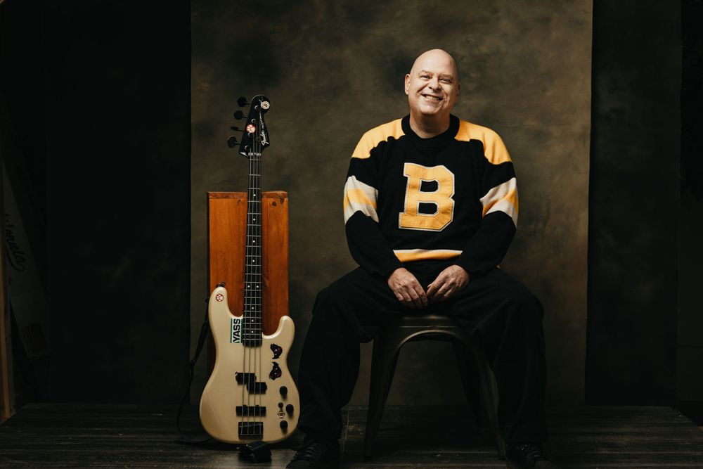 Professional headshot with guitar and musical instruments visible in background.