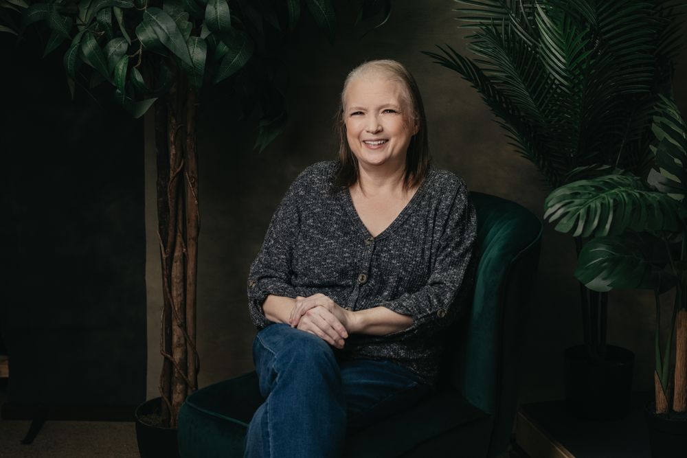Professional studio portrait with moody lighting and green palm leaves in background.