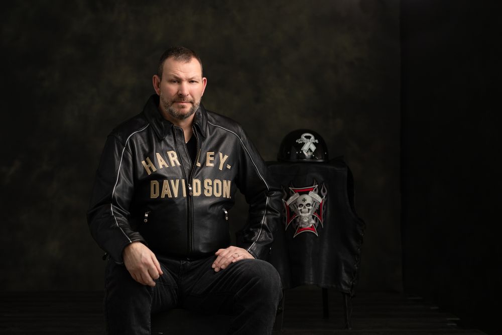 Dark studio portrait with dramatic lighting against textured background.