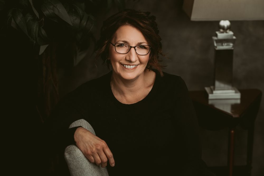 Studio portrait featuring glasses and black attire against dark background.