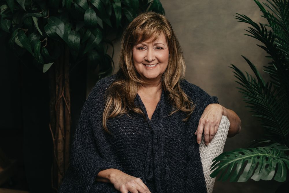 Portrait session with tropical plants and natural lighting against neutral wall.