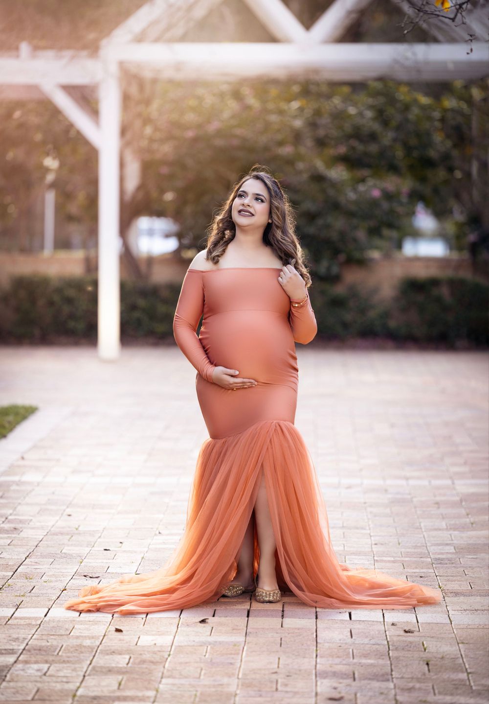 Maternity photo of an elegant coral gown with flowing tulle skirt against a softly lit outdoor backdrop.