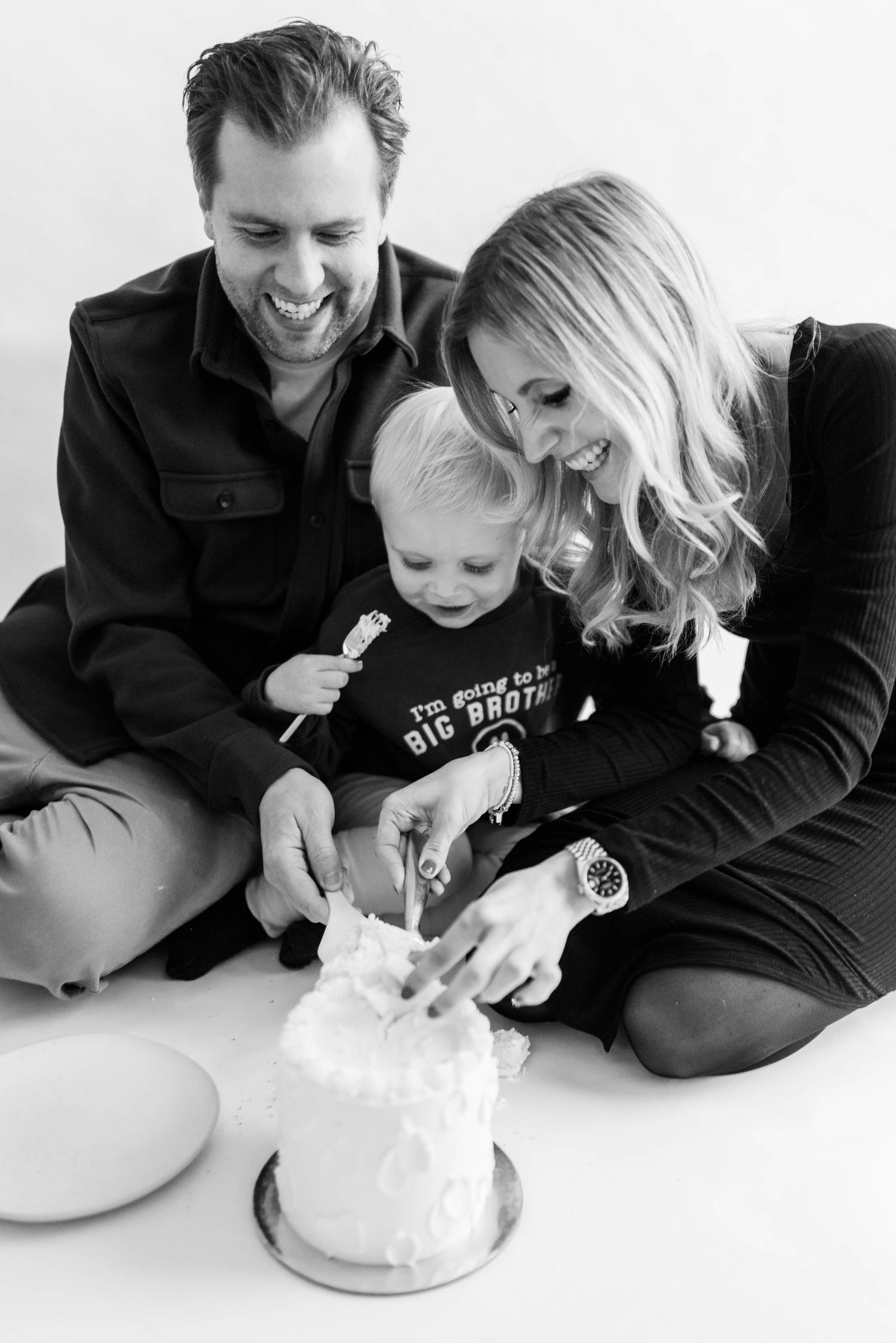A family enjoys a candid moment together with a small cake in black and white.