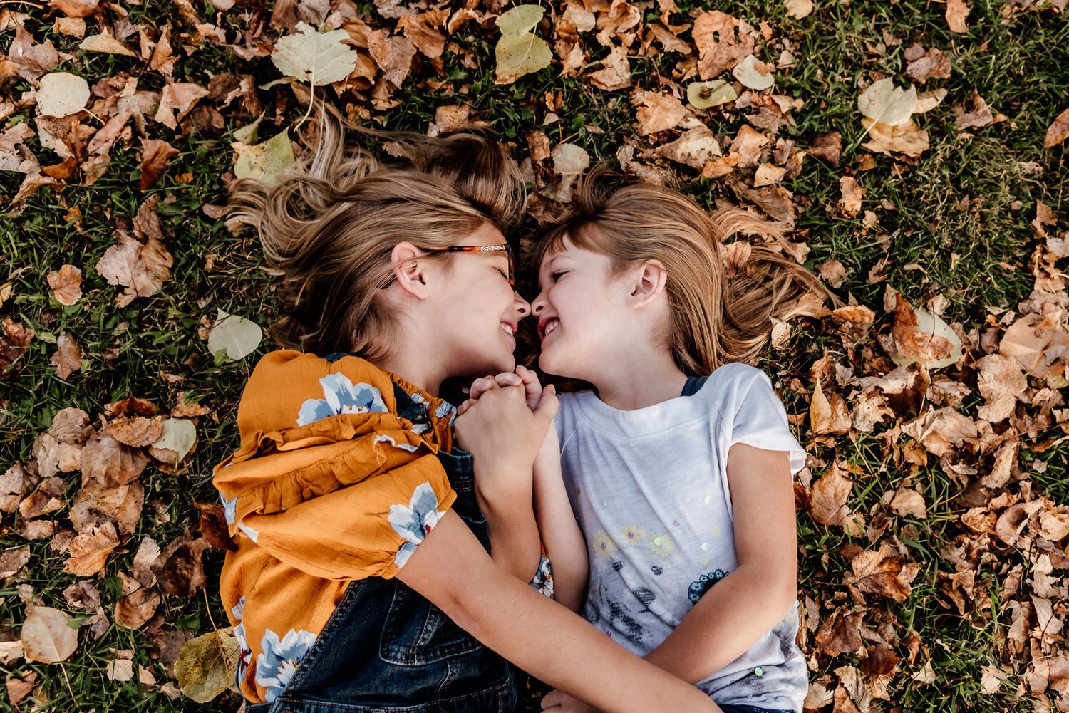 Two children lying on autumn leaves smiling and laughing together.