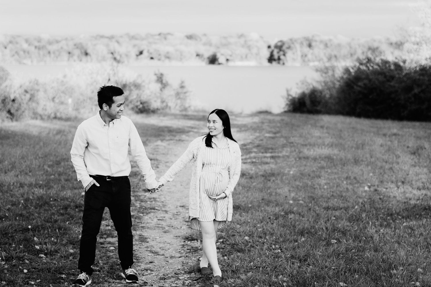 man and woman holding hands walking in field with lake in background