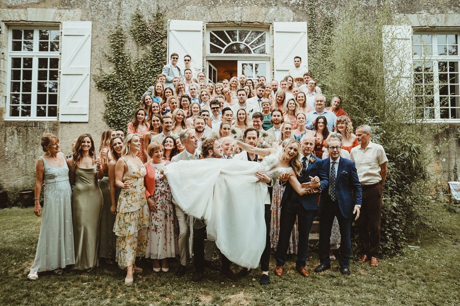 Large wedding party poses for group photo outside a charming French countryside chateau.